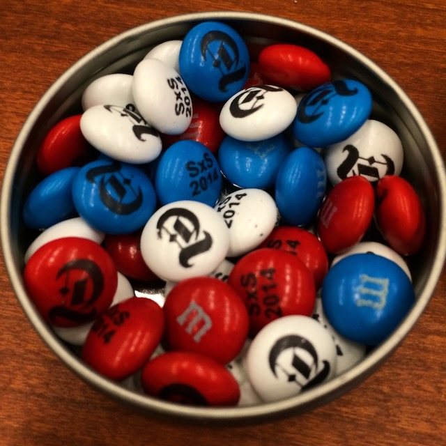 A small circular tin of red, white and blue M&Ms each with a gothic T from the New York Times log
