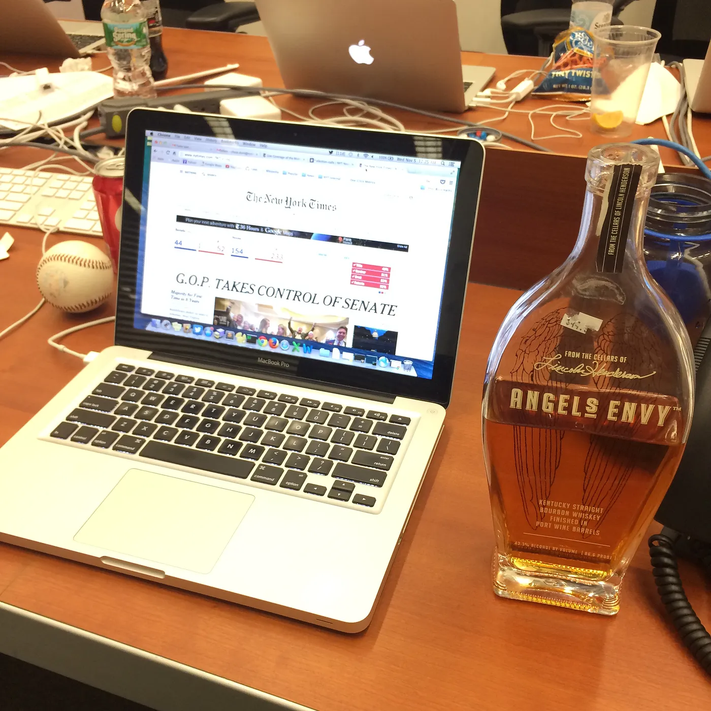 A square picture showing a conference table. On the left is a laptop with the New York Times website on it and the headline GOP Takes Control of the Senate. On the right is a half-empty bottle of Angels Envy bourbon.