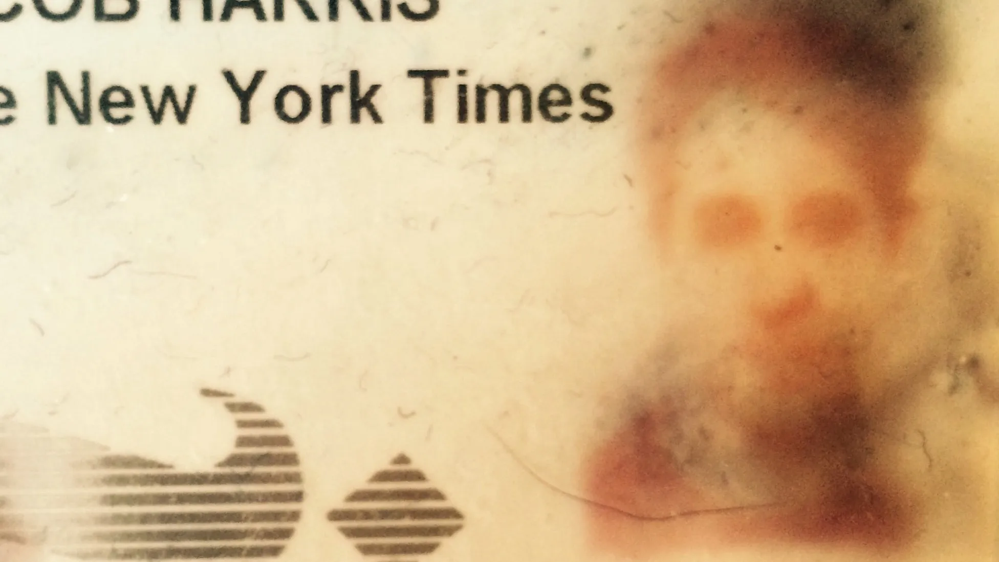 A closeup photo of a corporate ID badge for the New York Times. It shows the name Jacob Harris and a photo with a weird ghostly and distorted image as most of the ink had been rubbed off in a wallet over time.